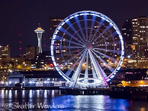 the ferris wheel is lit up at night in front of the seattle skyline and ...