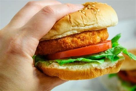 a hand holding a chicken sandwich with lettuce and tomatoes