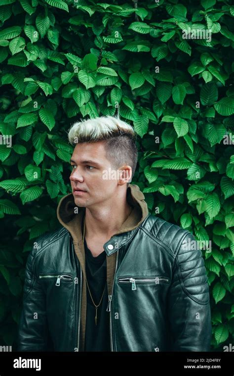 young man with platinum blonde hair and black leather jacket, ivy greenery background Stock ...