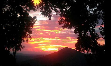 the sun is setting behind some trees on top of a hill with mountains in ...