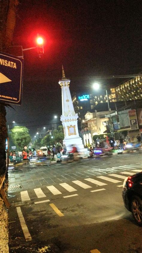 a car driving down a street next to a tall white tower with a clock on it's side