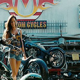 a woman standing next to motorcycles in front of a sign that says motor cycles on it