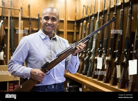 Happy hispanic man standing with hunting rifle at gun shop Stock Photo ...