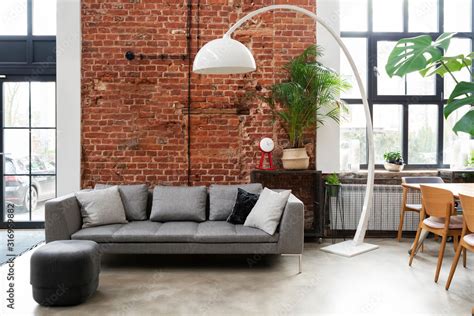 Living room interior in loft apartment in industrial style with brick wall, grey stylish sofa ...