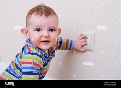 Baby toddler reaches into the electrical outlet on the home wall with his hand. Danger and ...