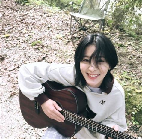 a young woman sitting on the ground holding an acoustic guitar