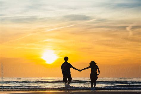 Silhouettes of man and woman holding hands on the beach at sunset by ...