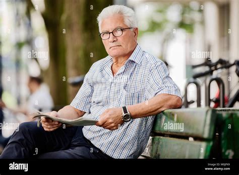 Grauhaariger senior sits in Cologne's Old Town on a bank and reads a newspaper, Cologne, North ...