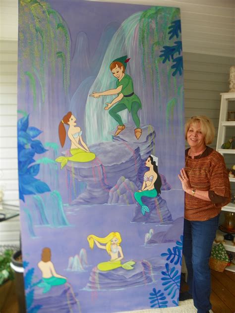 a woman standing in front of a painting on the side of a wall with mermaids