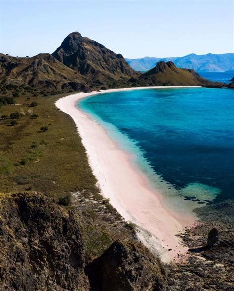 an island with white sand and blue water in the ocean next to some mountain range