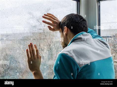 Depressed young man upset with bad news looking through rainy window glass Stock Photo - Alamy