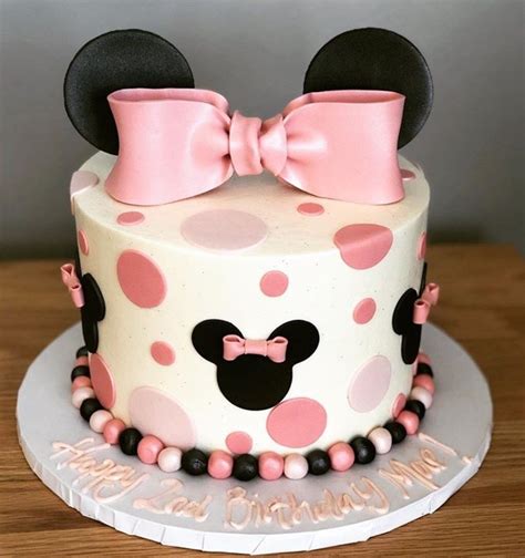 a minnie mouse birthday cake with pink and black polka dots on the top, topped with a bow