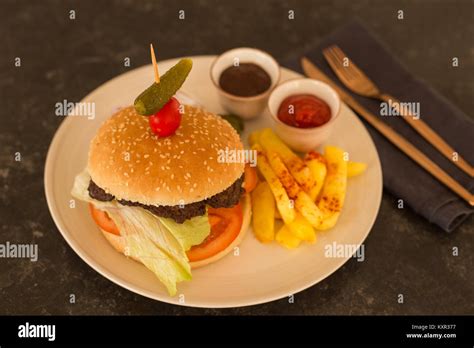 Hamburger with french fries, tomato and barbeque sauce in a beige ceramic plate placed on black ...