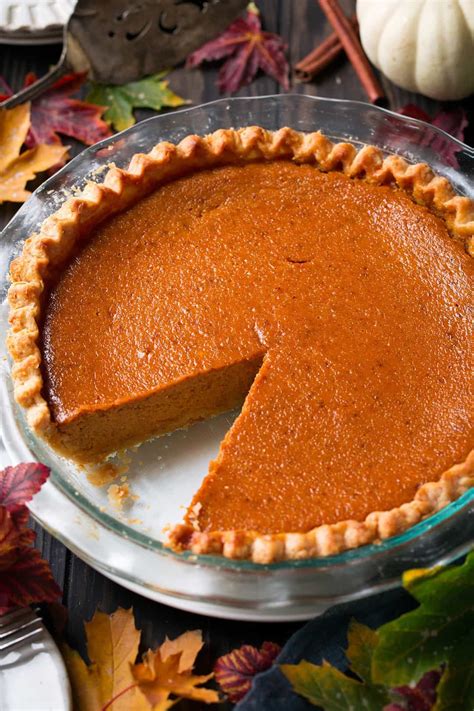 a pie sitting on top of a glass plate next to autumn leaves and pumpkins