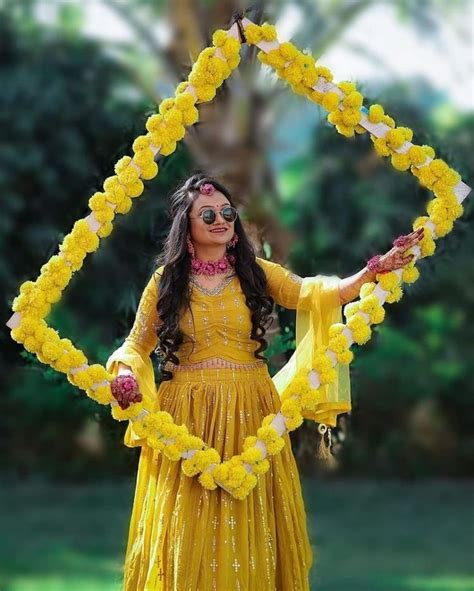 a woman in a yellow dress with flowers on her head and arms, holding a flower arch