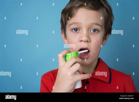 Caucasian boy sprays an aerosol into his mouth to treat sore throat ...