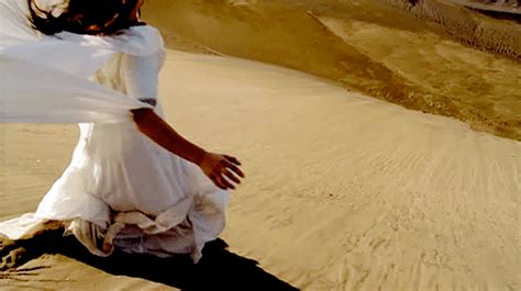a woman in a white dress is running across the sand dunes with her arms outstretched