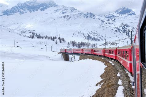 Bernina mountain pass. The famous red train is crossing the white lake. Amazing landscape of the ...