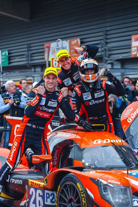 two men standing on top of an orange race car in front of a group of people