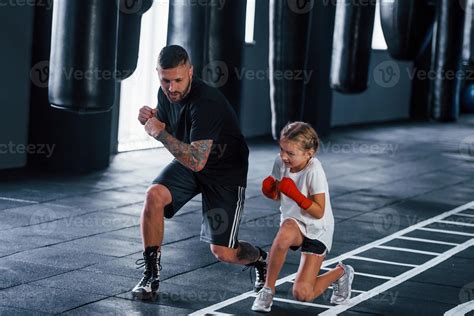 golpes básicos. joven entrenador de boxeo tatuado enseña a una linda niñita en el gimnasio ...