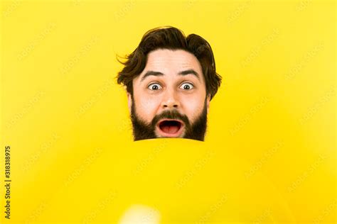 surprised bearded man looking at camera while peeking out from above ...