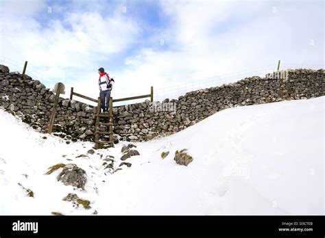 Male walker climbing over a stone stile at Ewe tarn, above Malham Cove ...