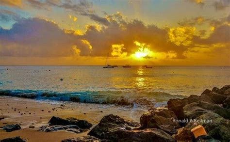 the sun is setting over the ocean with rocks on the beach and boats in ...