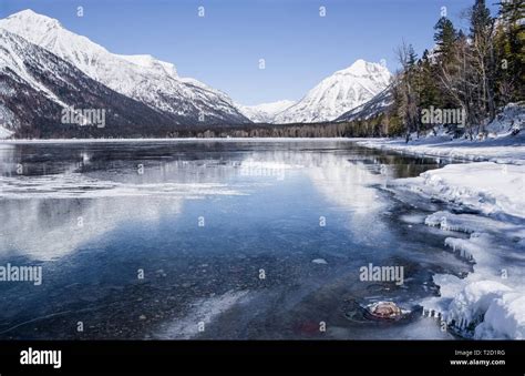 Montana Lake in Winter: Snow covered mountains reflect from the icy surface of Lake McDonald in ...