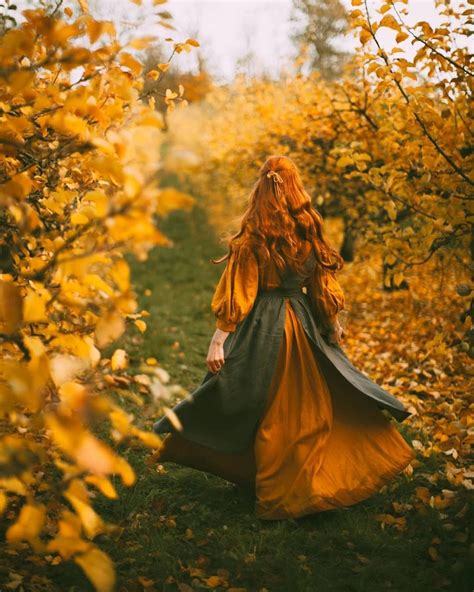 a woman with red hair is walking through the woods in an orange and green dress