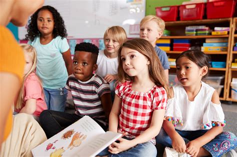 Group Of Elementary School Pupils Sitting On Floor Listening To Female ...