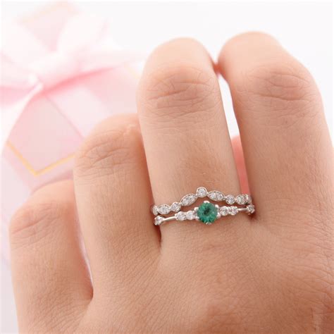 a woman's hand holding a ring with an emerald and white diamonds on it