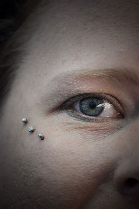 a woman's eye with piercings on her forehead and eyeshade in front of her face