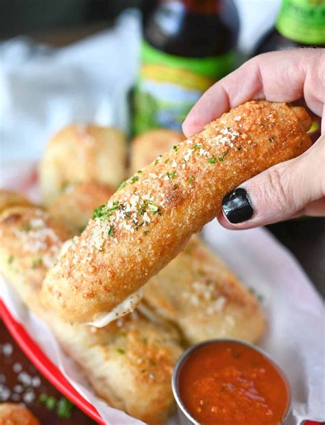 Stuffed pepperoni breadstick being picked up from a red serving basket with a side of pizza ...