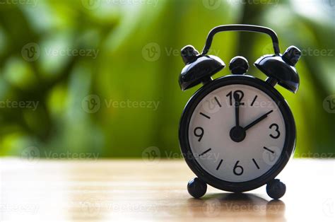 Alarm clock pointing at 2pm with blurred nature background. With ...