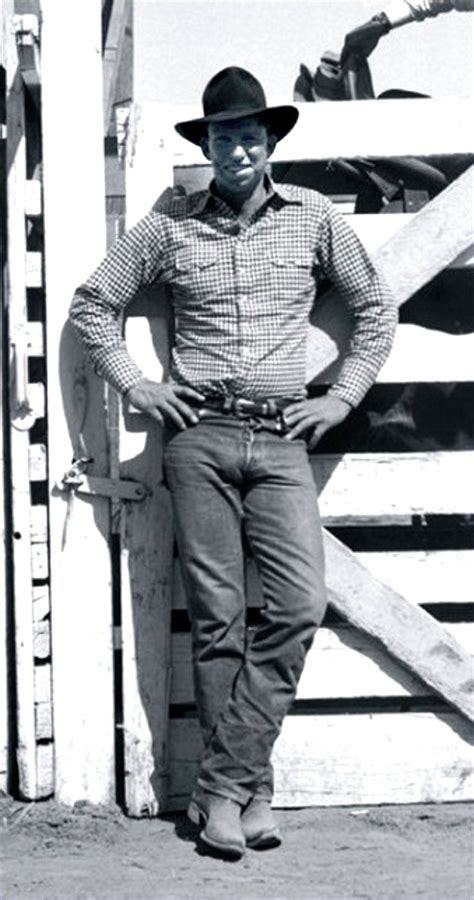 a man in a cowboy hat leaning against a fence