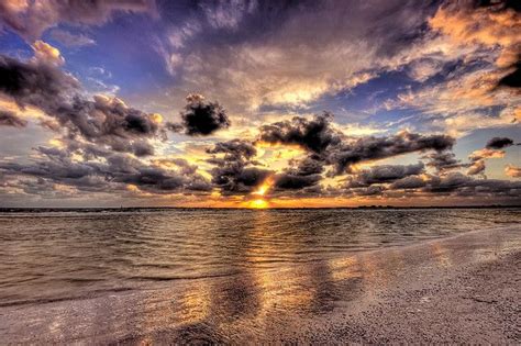 the sun is setting over the ocean with clouds in the sky and sand on the beach