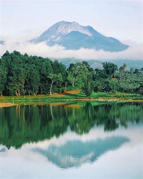 a lake surrounded by lush green trees with a mountain in the backgroup