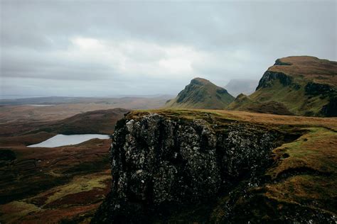 view of a cliff overlooking mountains a lake overcast skies and brown grass, cliff edge and ...