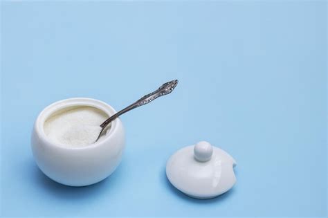 Premium Photo | Open white sugar bowl with a spoon inside and a lid next to it on a blue ...