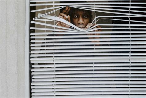 Young man looking out of window blinds at home stock photo