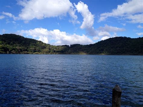 a body of water with hills in the distance and clouds in the sky above it