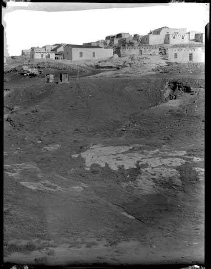 an old black and white photo of some buildings on a hill with dirt in the foreground