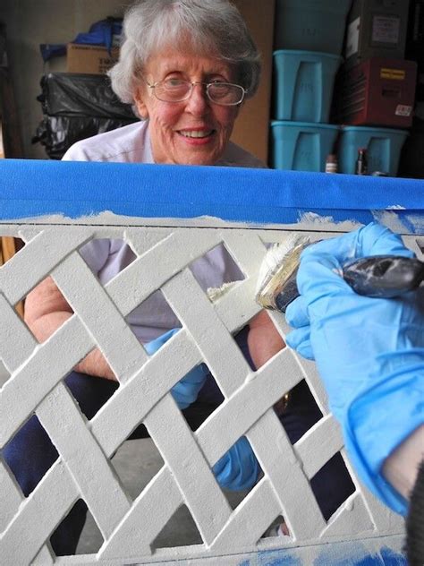 an older woman is painting a fence with white paint and blue tape on the sides