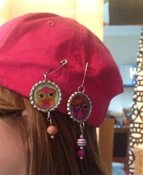 a woman wearing a red hat with owl charms on it's ear and earrings hanging from the side