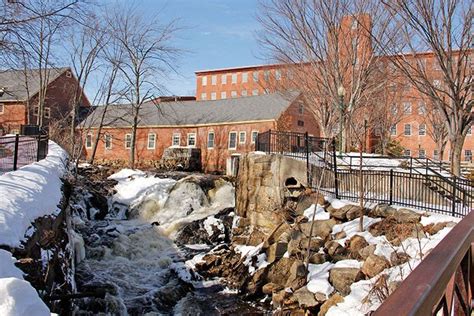 a river running through a snow covered park next to tall brick buildings with trees in the ...