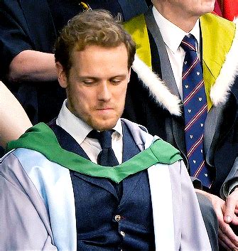 a man wearing a green and white graduation gown sitting in front of ...
