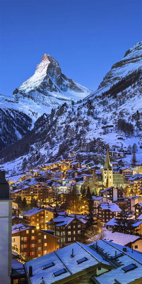 a snowy mountain is in the background with buildings and lights on it, as well as snow - capped ...
