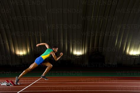 Young woman sprinting from starting blocks in stadium stock photo