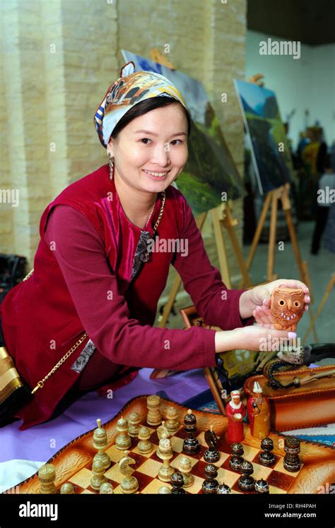 Asian woman standing at a table set with traditional Kazakh souvenirs showing them to visitors ...