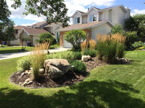 Front yard berm with round boulders, wood mulch, and plants | The Lawn Salon